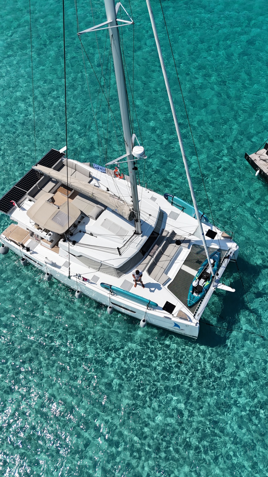 Aerial view of HONU MOANA at anchor over clear turquoise water with paddleboards and kayak on deck